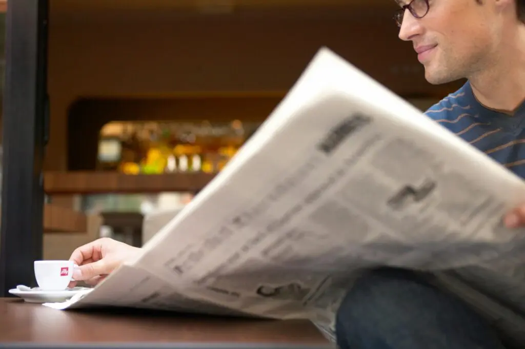 A man sitting at a table reading a newspaper.